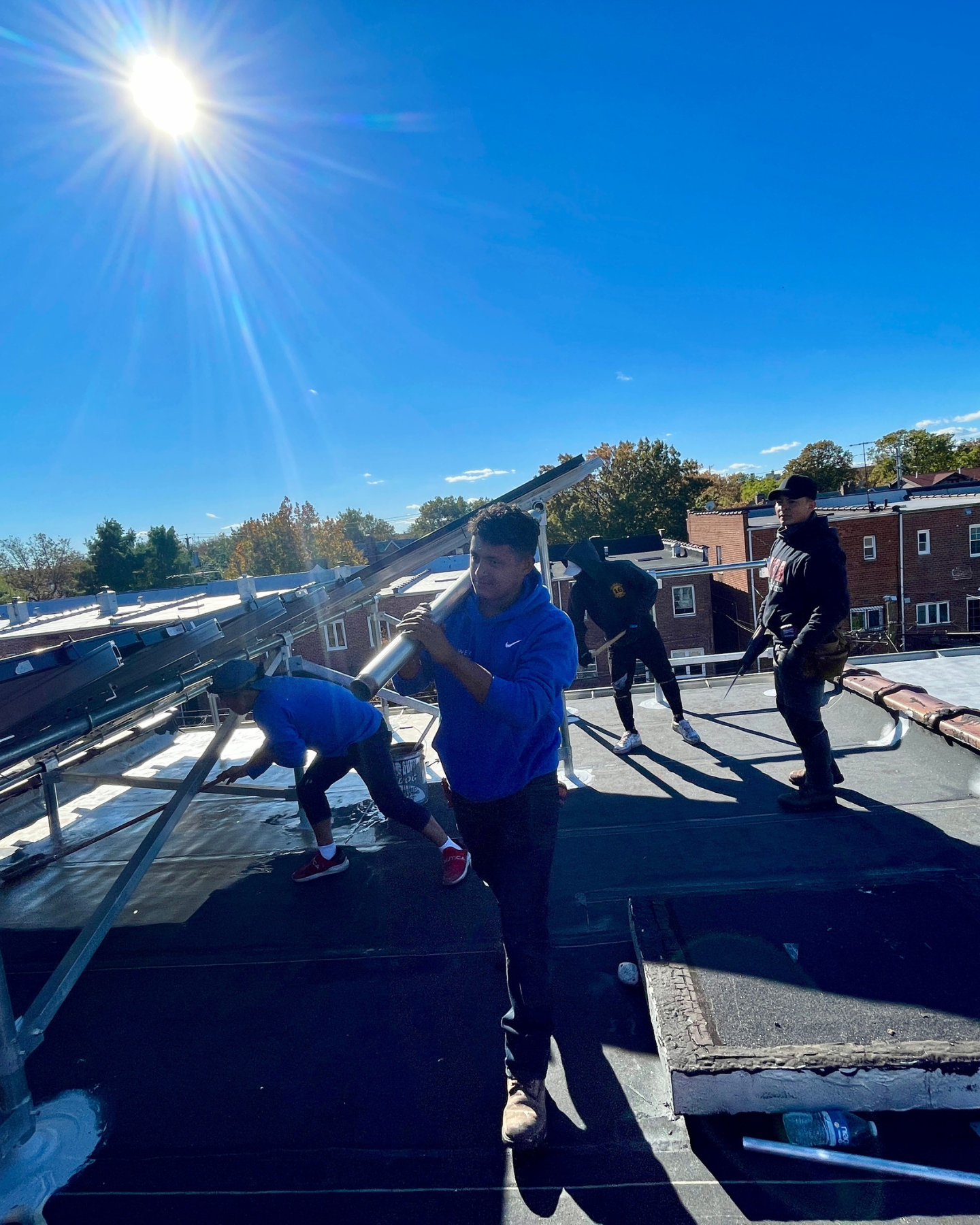 Kamtech Solar installation team working on rooftop under bright sun, carrying solar mounting equipment and assembling a solar panel system for clean energy production.