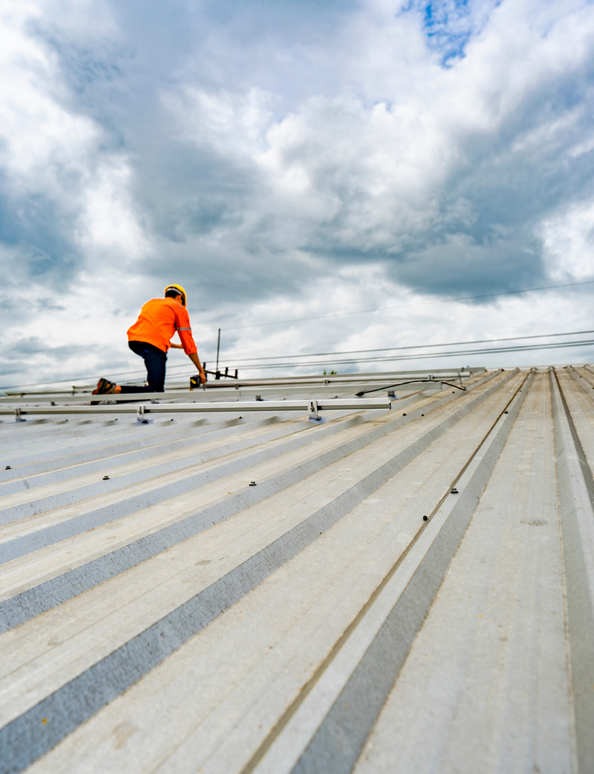 Kamtech Solar technician installing a rooftop solar mounting system on a metal roof under a cloudy sky, showcasing professional solar installation and a clean energy setup. Kamtech Solar technician installing a rooftop solar mounting system on a metal roof under a cloudy sky, showcasing professional solar installation and a clean energy setup.